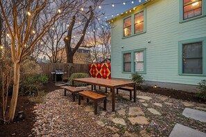 Une terrasse avec une table et des bancs en bois, un barbecue et des guirlandes lumineuses.