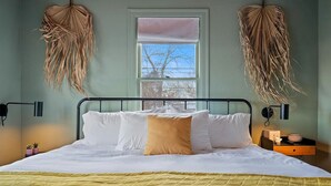 Un letto con lenzuola bianche e gialle, una finestra con vista e due piante pensili.