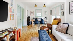 A living room with a sofa, a coffee table, a dining table with chairs, a TV, and artwork on the walls. - Ted & Breakfast • Cozy East Austin Retreat (Austin)