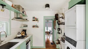 A kitchen with a stove, sink, and shelves with kitchenware. - Ted & Breakfast • Cozy East Austin Retreat (Austin)