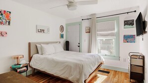 A bedroom with a bed, a ceiling fan, a window with curtains, and a TV mounted on the wall. - Ted & Breakfast • Cozy East Austin Retreat (Austin)