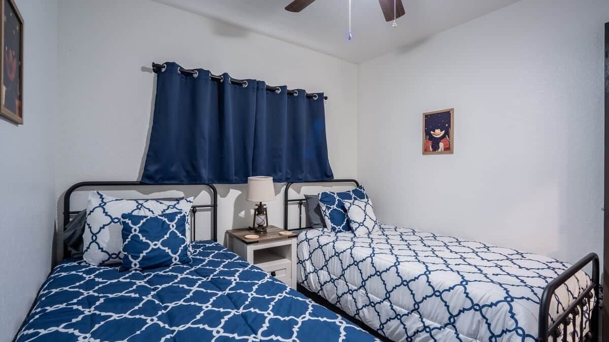 A bedroom with two beds, a nightstand, a lamp, and a ceiling fan.