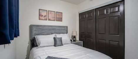 Ein Schlafzimmer mit einem Bett, einem Nachttisch, einer Lampe und einem dunklen Holzschrank.