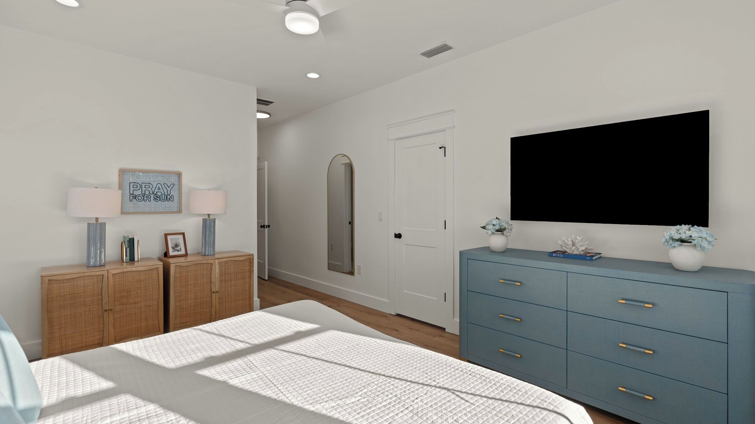 A bedroom with a bed, bedside tables, a dresser, a mirror, and a TV.