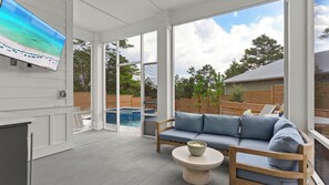A covered patio with a pool, a sofa, and a table. - 30A Southern Sugar by Avantstay Sleeps 26 Pool + Hot Tub + Game Room + Golf Cart + Bikes (Santa Rosa Beach)