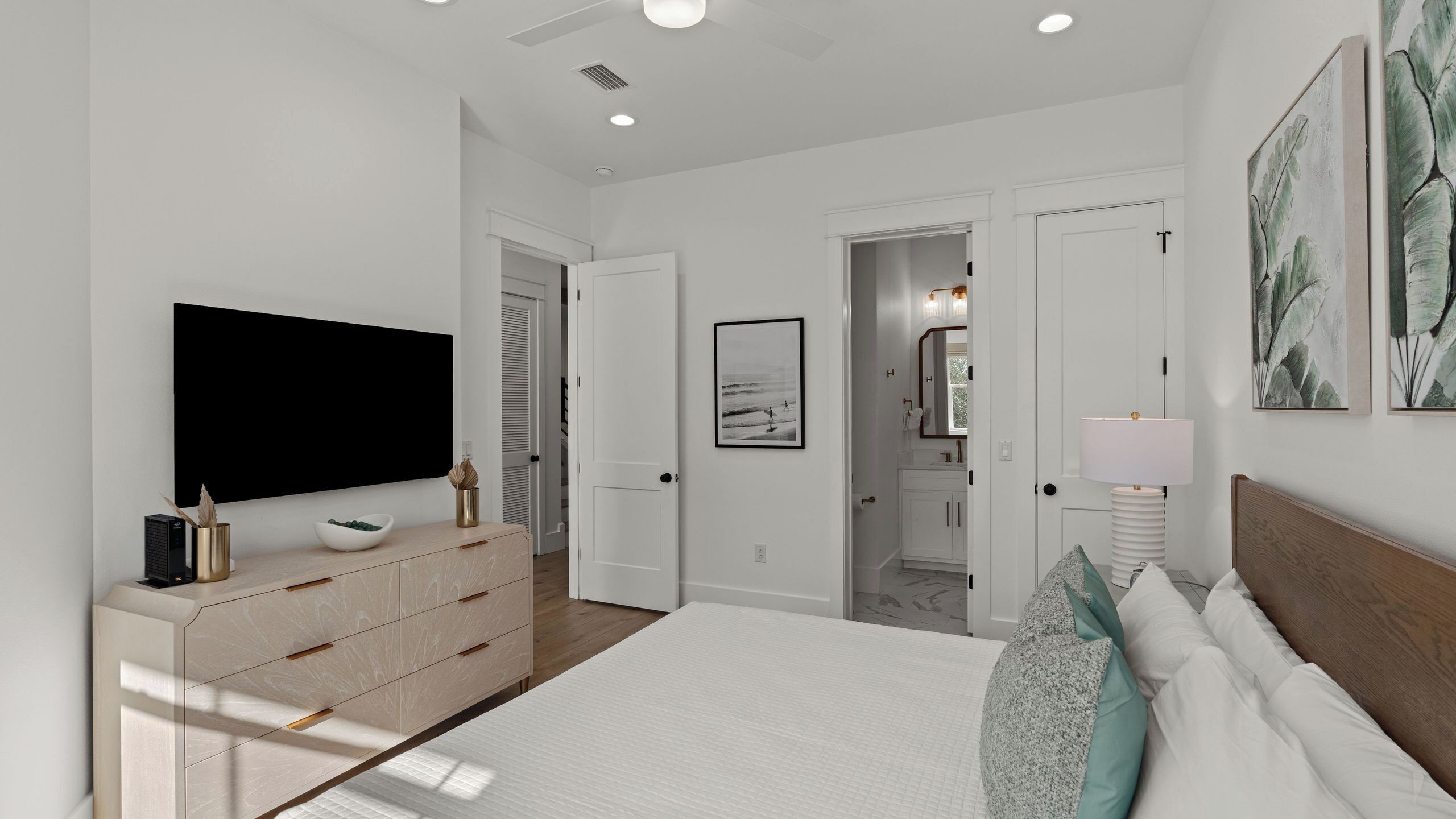 Un dormitorio moderno con una cama grande, un aparador, un televisor de pantalla plana y un baño a la vista a través de una puerta abierta.
