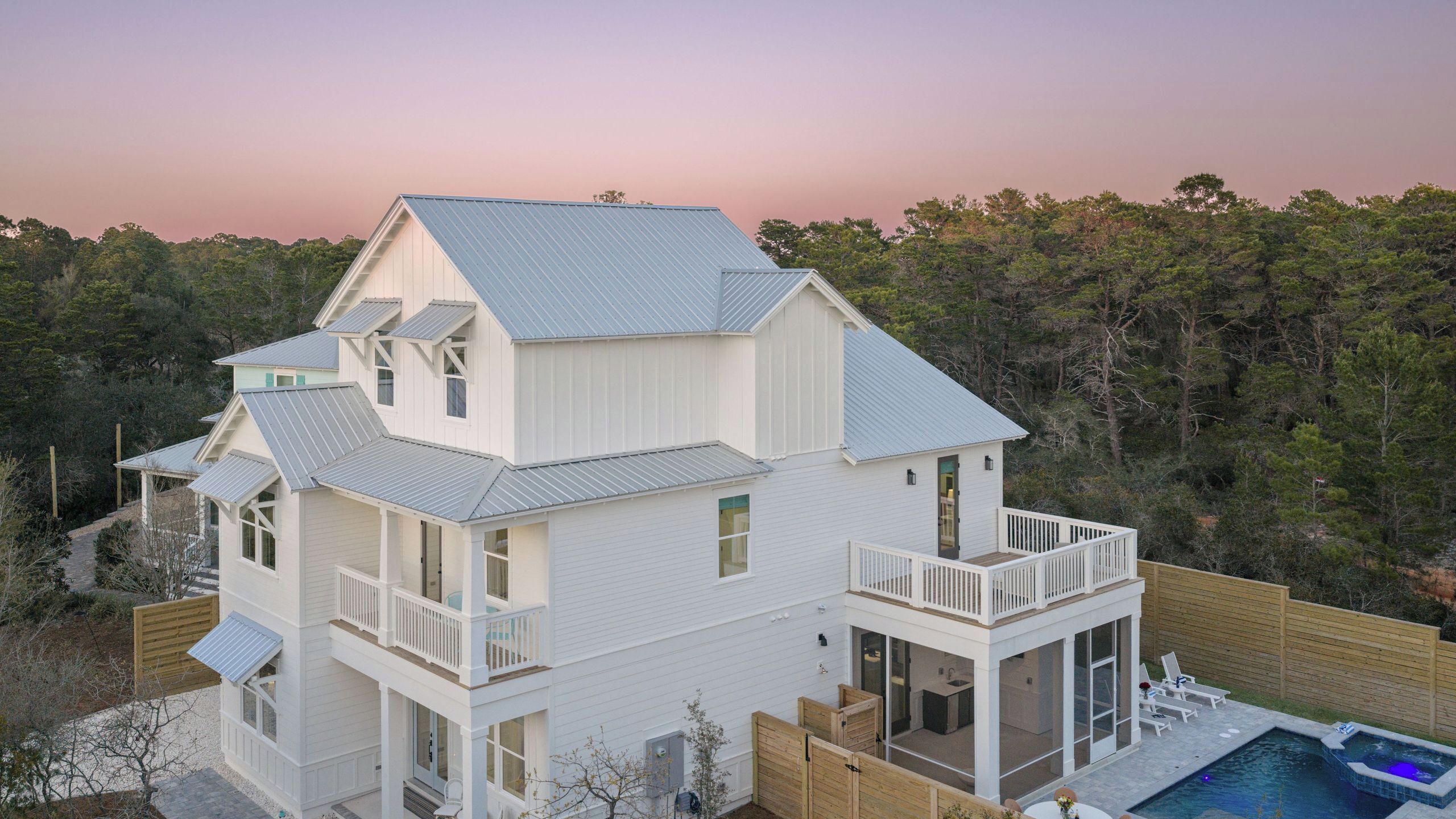 A two-story house with a balcony, a swimming pool, and a view of the surrounding forest.