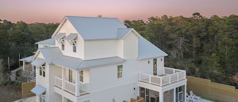 A two-story house with a balcony, a swimming pool, and a view of the surrounding forest.