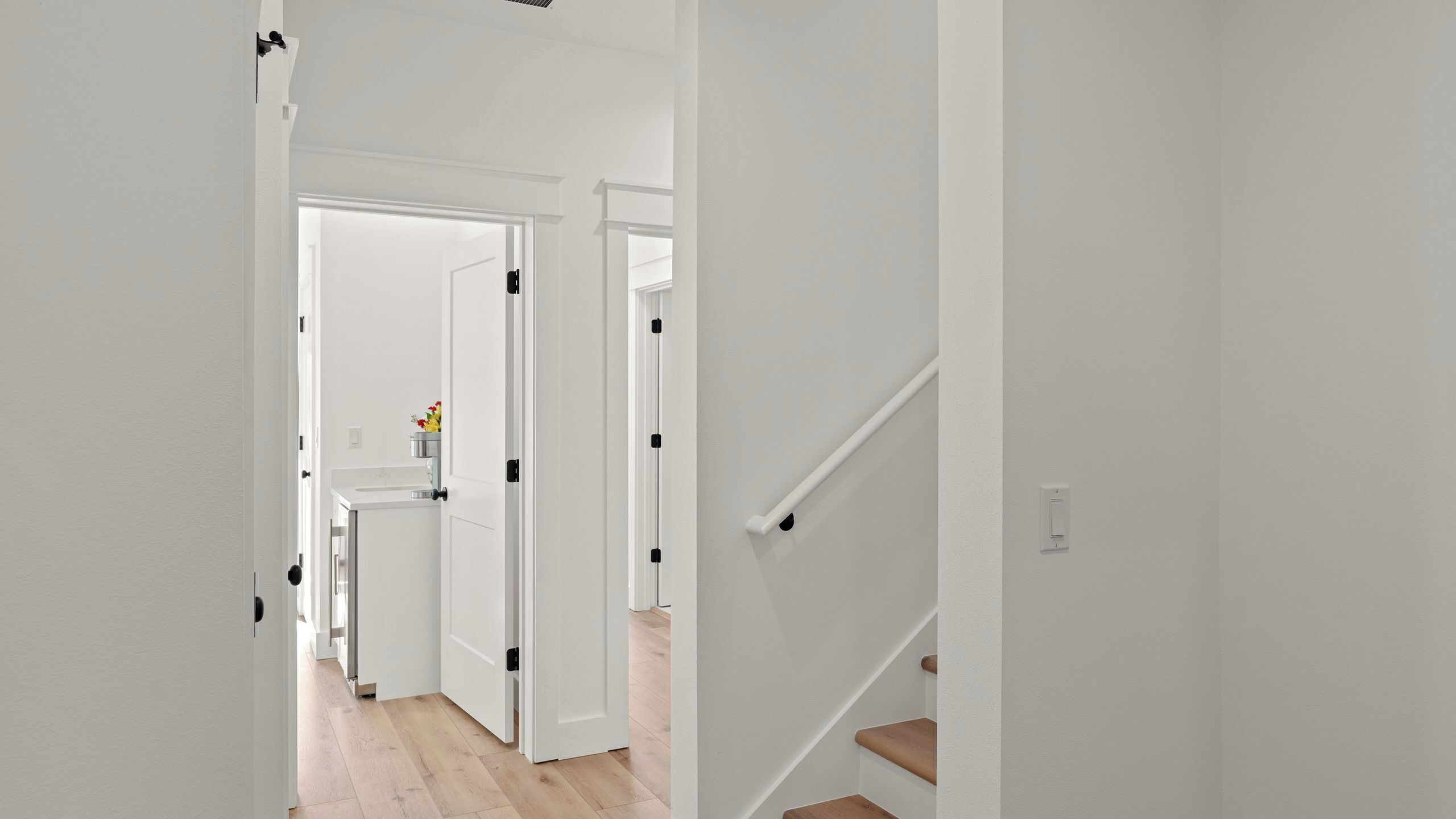 A hallway with white walls, a wooden floor, and a staircase with wooden steps.