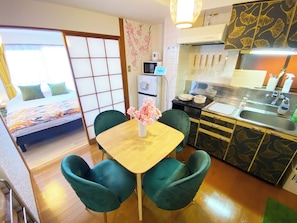 A compact hotel room with a bed, a small kitchenette, a dining area with a table and chairs, and a sliding shoji screen door.