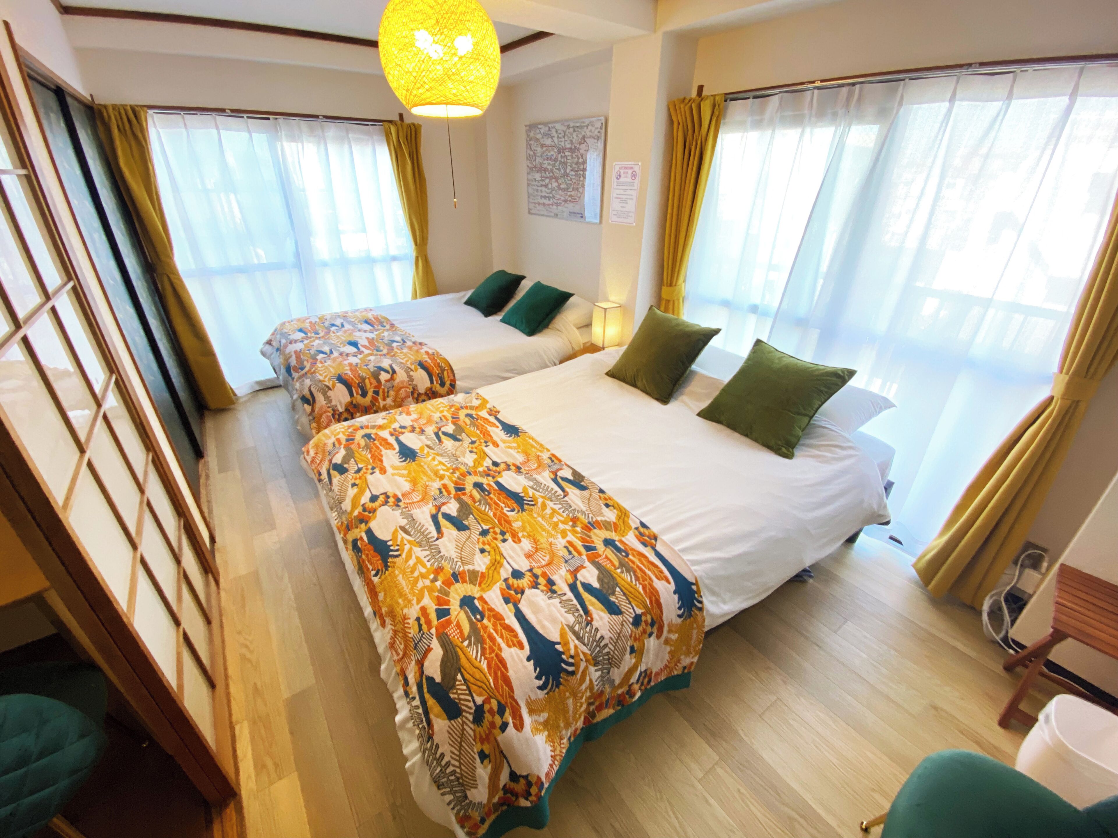 A hotel room with two beds, a wooden floor, a hanging light fixture, and a window with curtains.