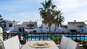 Zona de piscina con mesa, sillas y vistas a edificios blancos y palmeras.