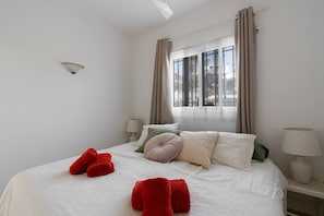 A bedroom with a bed, two bedside tables, a window with curtains, and a wall-mounted light fixture. - Capistrano Village, 1 bedroom (Nerja)