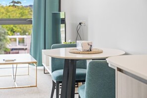 A modern room with a round table, teal chairs, and a view of greenery outside. - Spacious 1BR Apartment | Walk to Tram | Parking (Dickson)