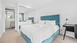 Une chambre d’hôtel moderne avec un grand lit, un bureau et une salle de bain visible à travers une porte ouverte.