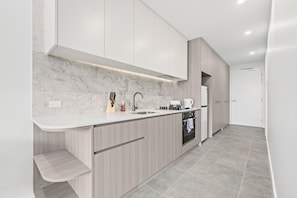 A modern kitchen with a marble backsplash, wooden cabinets, a built-in oven, and a white countertop. - Spacious 1BR Apartment | Walk to Tram | Parking (Dickson)