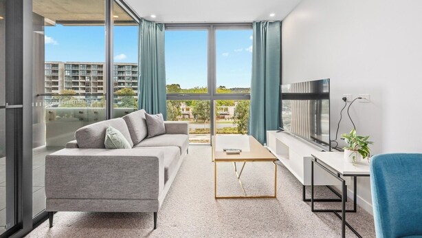 Un salon moderne avec un canapé, une table basse, un téléviseur et une vue sur un quartier résidentiel.