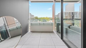 Un balcon doté d’une balustrade en verre, d’un banc rembourré et offrant une vue sur les bâtiments environnants.