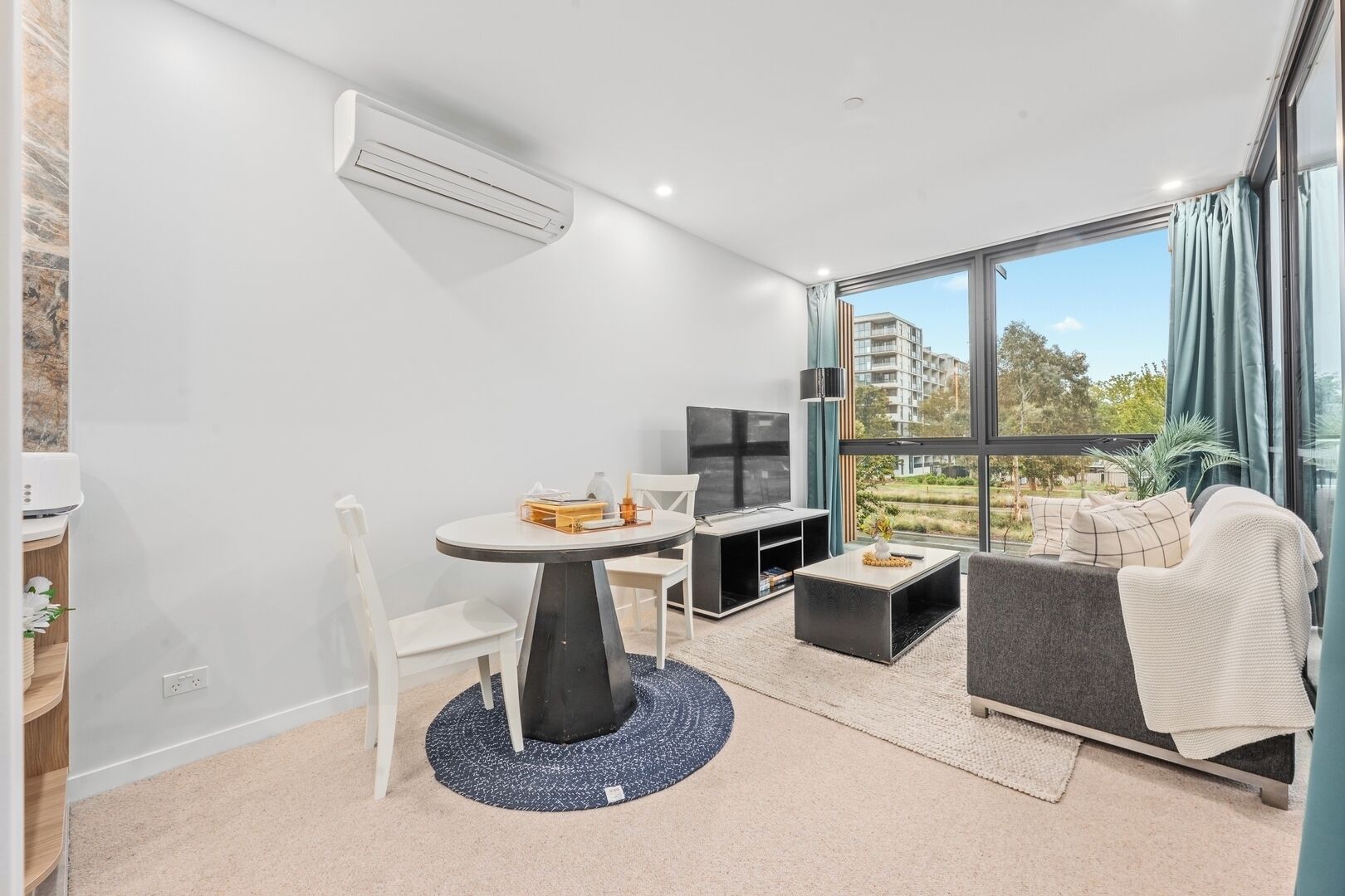 A modern living room with a dining area, a flat-screen TV, and a large window with a view of the city.