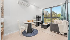 Een moderne woonkamer met een eethoek, een flatscreen televisie en een groot raam met uitzicht op de stad.