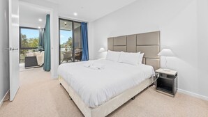 Een moderne slaapkamer met een groot bed, een nachtkastje, een lamp en uitzicht door een glazen deur op een zitgedeelte buiten.