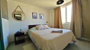 Une chambre à coucher avec un lit, une table de chevet, un miroir et deux tableaux encadrés accrochés au mur.