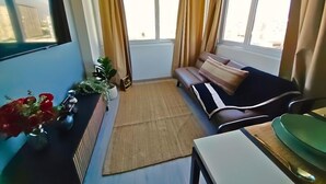 Un salon avec un canapé, une table basse, un téléviseur et une fenêtre avec des rideaux.