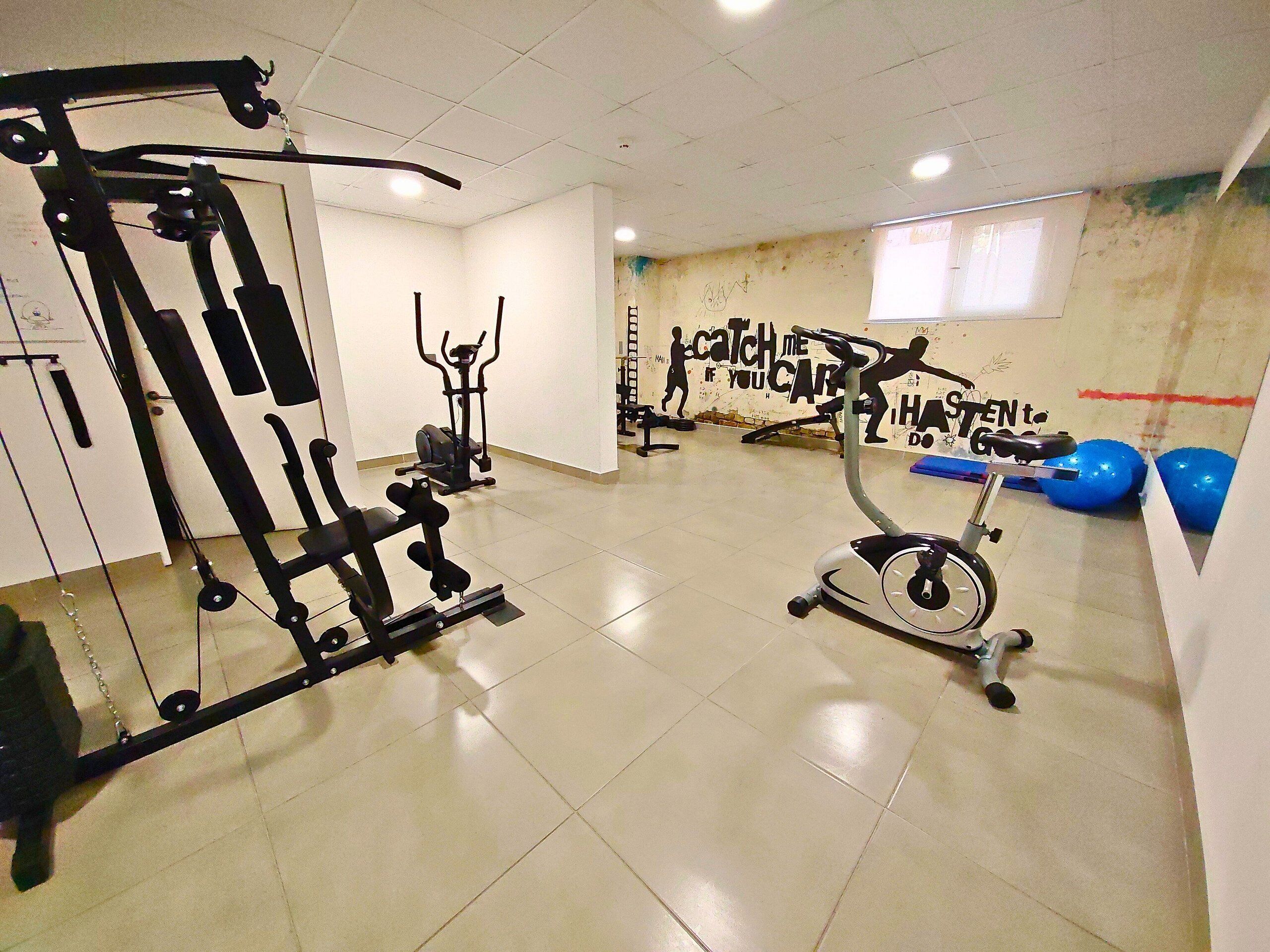 Ein Fitnessstudio mit verschiedenen Trainingsgeräten, einer Wand mit motivierenden Texten und einem Fenster.