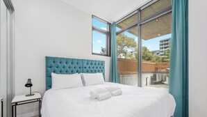 Een moderne hotelkamer met een groot bed, een nachtkastje met een lamp en uitzicht op buiten.