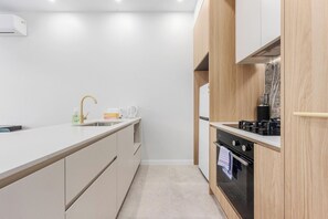 A modern kitchen with a white countertop, a sink, a stove, and wooden cabinetry. - Charming 2BR Apartment | Walk to Tram | Parking (Dickson)