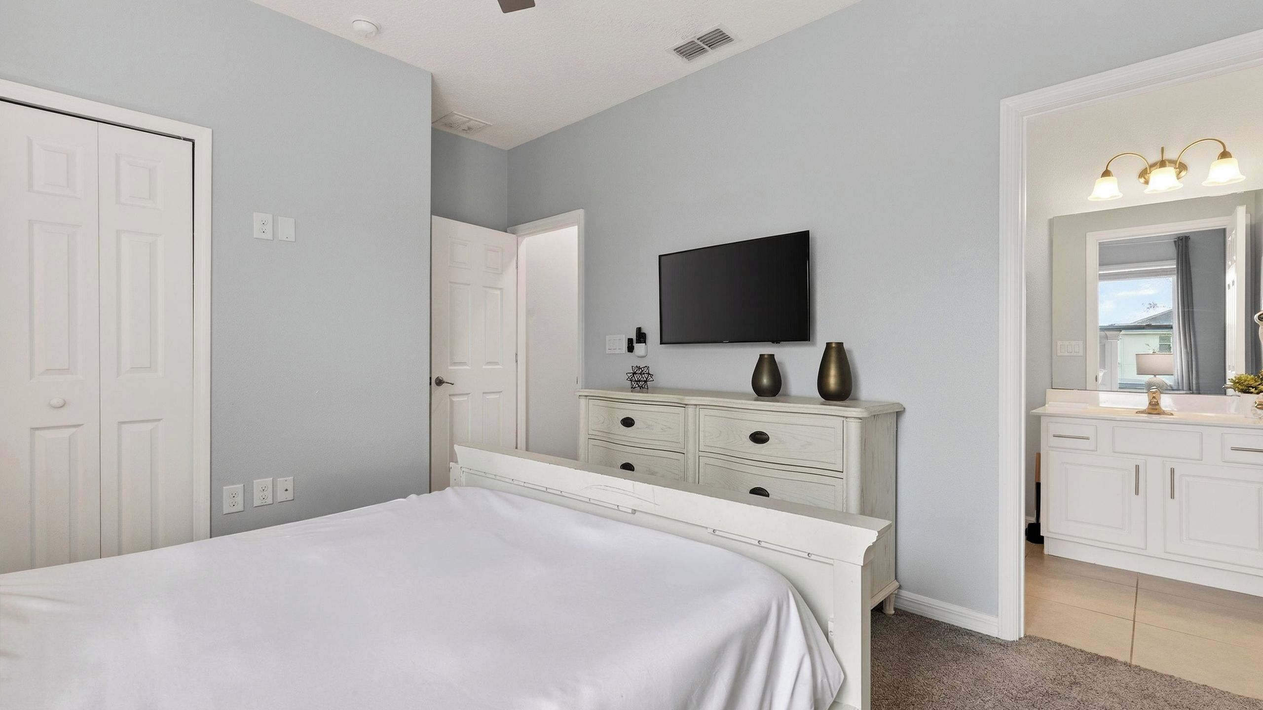 A bedroom with a bed, a dresser, a television, and a bathroom with a mirror and sink.
