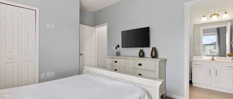 A bedroom with a bed, a dresser, a television, and a bathroom with a mirror and sink.