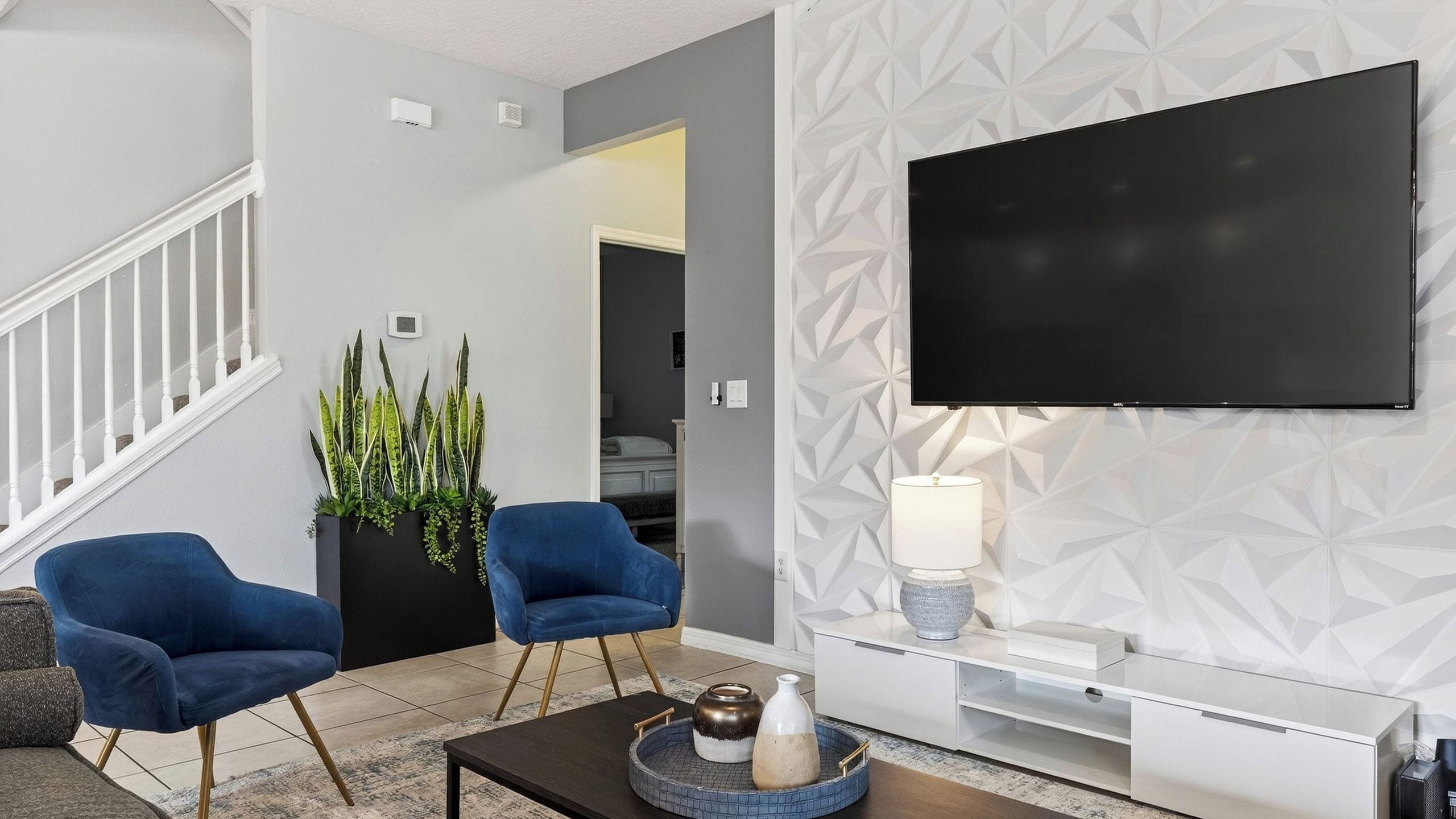 A modern living room with a flat-screen TV, two blue armchairs, a coffee table, and a decorative plant.