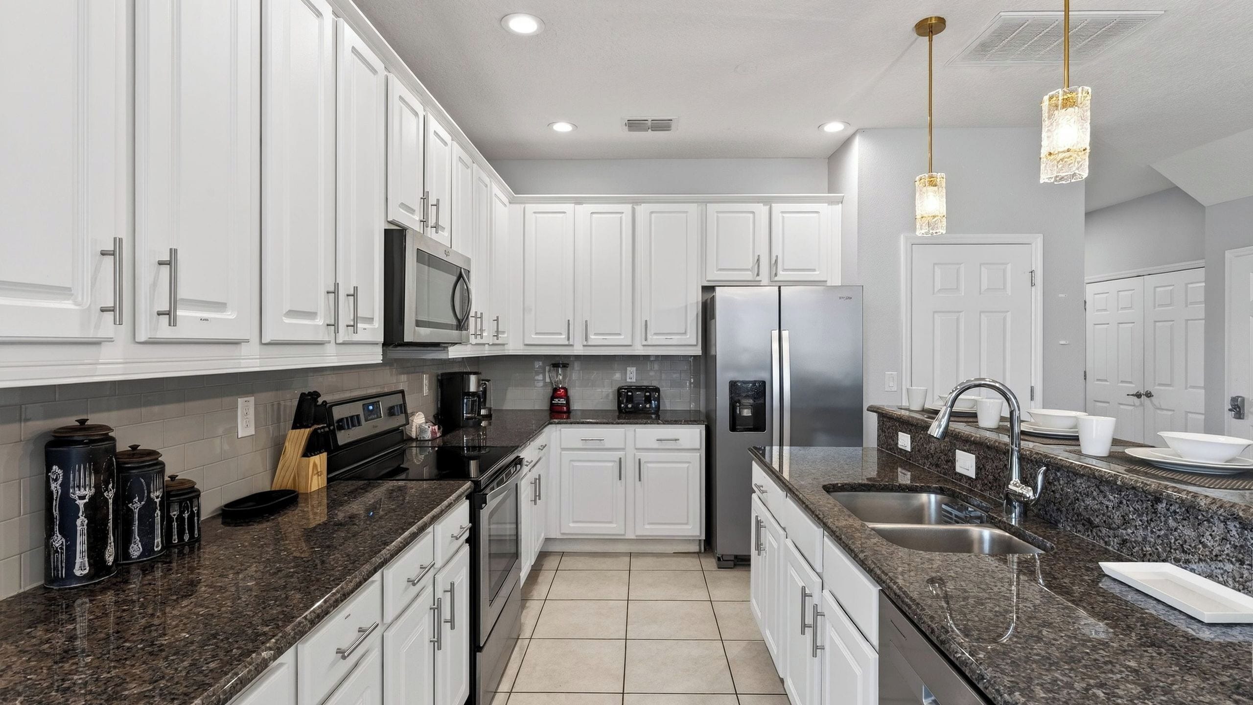 A modern kitchen with white cabinets, stainless steel appliances, granite countertops, and pendant lighting.