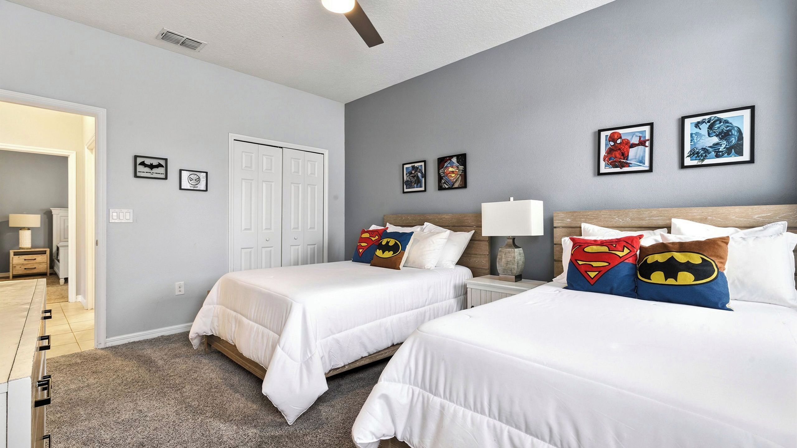 A bedroom with two beds, a nightstand, a lamp, and framed superhero artwork on the wall.