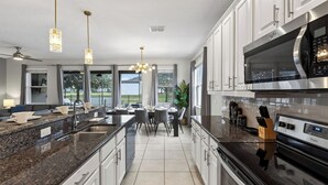 A modern kitchen with granite countertops, stainless steel appliances, and a dining area with a view. - Shiva by Avantstay Sleeps 22 Pool + Hot Tub + Great Park Access (Kissimmee)