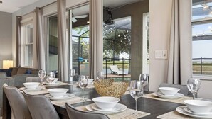 A dining area with a table set for six, large windows, and a view of the outdoors. - Shiva by Avantstay Sleeps 22 Pool + Hot Tub + Great Park Access (Kissimmee)