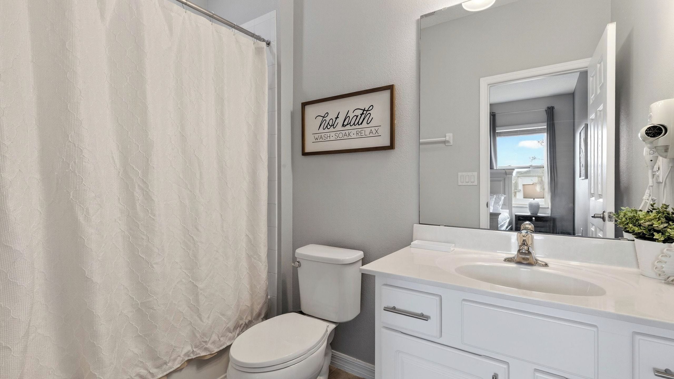 A bathroom with a toilet, a sink, a mirror, and a shower curtain.