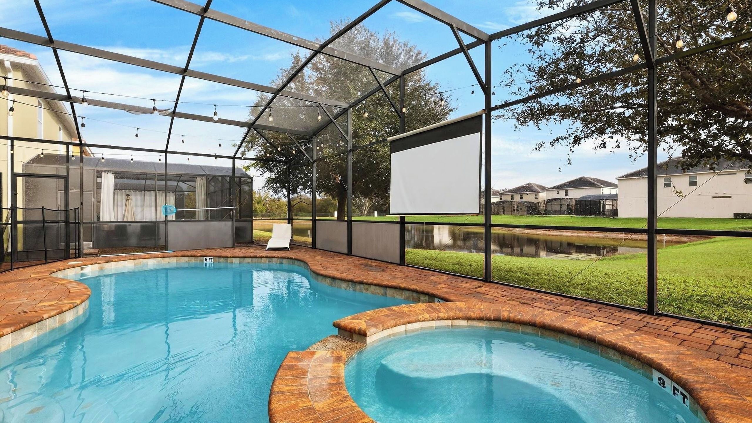 A swimming pool with a brick edge, a covered area with a whiteboard, and a view of houses in the background.