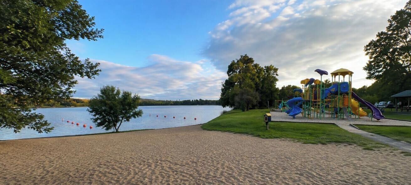 A sandy beach with a playground and a lake in the background.