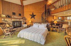 A cozy room with a fireplace, a bed, a rocking chair, and a staircase leading to an upper level.