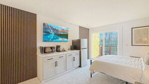 Une chambre à coucher comprenant un lit, une télévision, un four à micro-ondes, un réfrigérateur et une porte coulissante donnant sur un balcon.