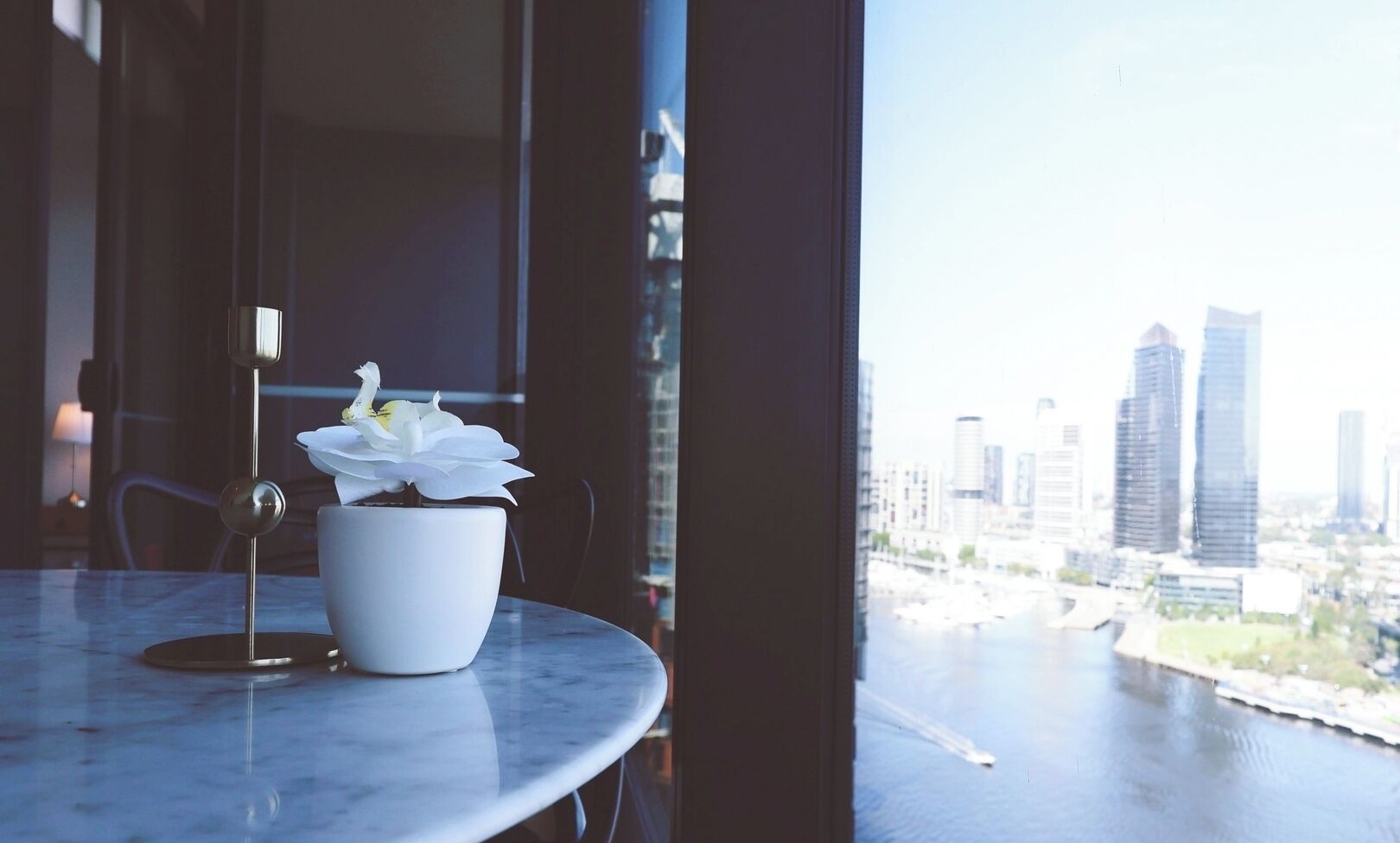 A potted orchid on a marble table by a window with a cityscape view.