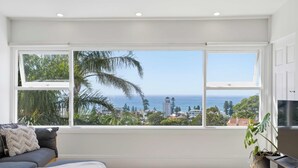 Een kamer met een groot raam, een grijze bank en een plant.