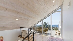 Een ruime kamer met een houten plafond, een wenteltrap en een balkon met uitzicht op zee.