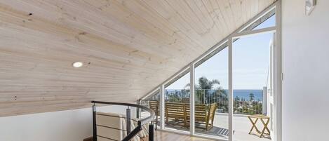 A spacious room with a wooden ceiling, a spiral staircase, and a balcony with a view of the sea.