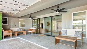 Eine großzügige Terrasse mit Holzmöbeln, Deckenventilatoren und einer großen Schiebeglastür, die zu einem Innenbereich führt.