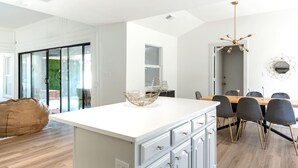 Eine moderne Küche mit Kochinsel, einem Essbereich mit Holztisch und -stühlen sowie einem großen Fenster für natürliches Licht.