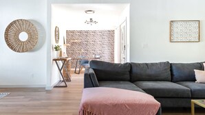 Ein modernes Wohnzimmer mit einem dunkelgrauen Sofa, einer rosafarbenen Decke und einer Ziegelwand.
