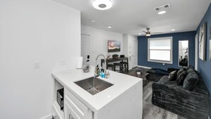 Een moderne keuken met een centraal eiland, een zithoek met tafel en stoelen, en een woongedeelte met een bank.